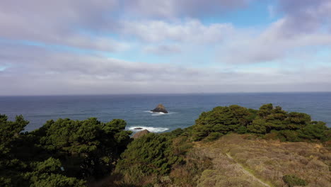 drone forward shot over port orford heads in southern oregon, usa during day with blue sky and clouds