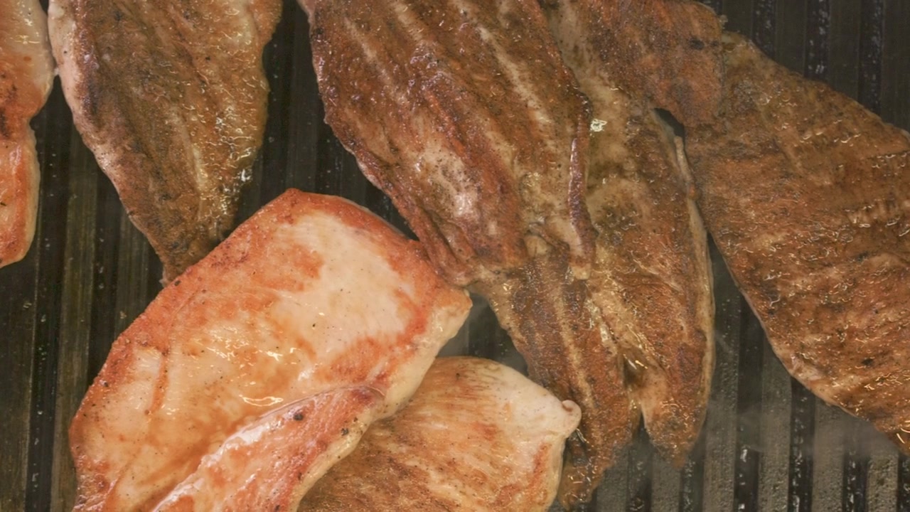 Una vista dall'alto cattura filetti di pollo sfrigolanti su una piastra, mettendone in risalto le ricche consistenze, i segni della griglia e i bordi caramellati durante la cottura