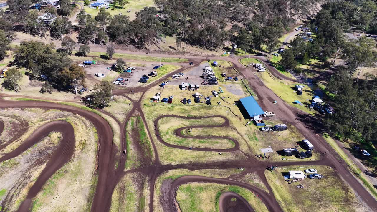 Drone captures winding motocross track, riders, vehicles, and spectators under bright daylight in Warwick
