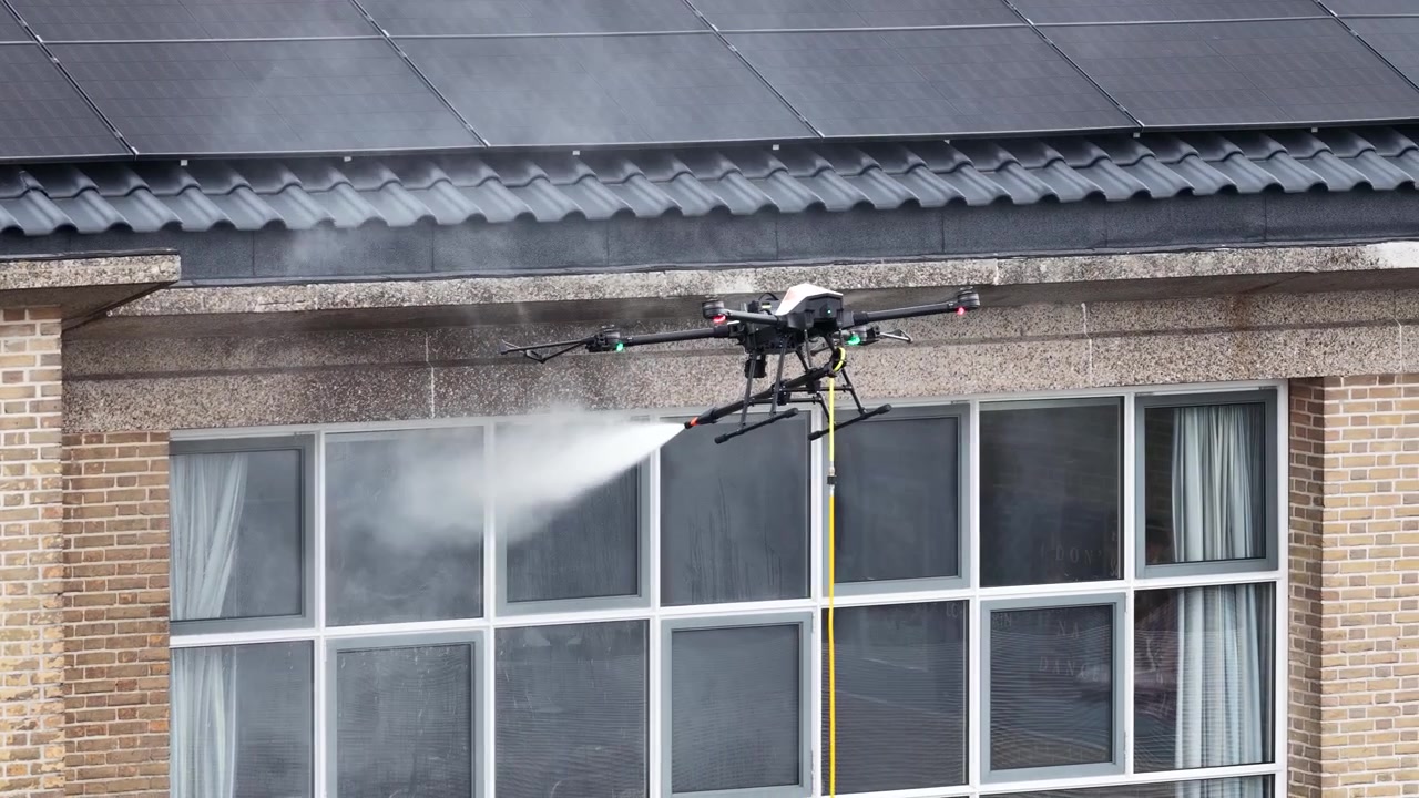 Drone équipé d'une buse haute pression pulvérisant de l'eau pour laver les vitres extérieures d'un immeuble de bureaux moderne, représentant l'avenir du travail de maintenance automatisé.