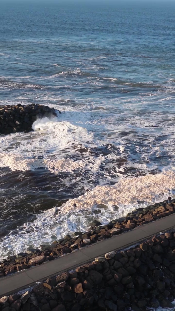 Onde oceaniche dinamiche si infrangono contro una costa rocciosa sotto cieli sereni, riprese con luce naturale e una telecamera stabile