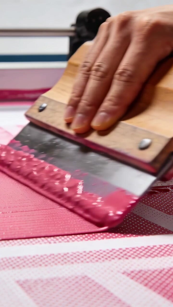 Vertical video: Starting tech bare arm pulling squeegee across screen in shop, printing pink ink