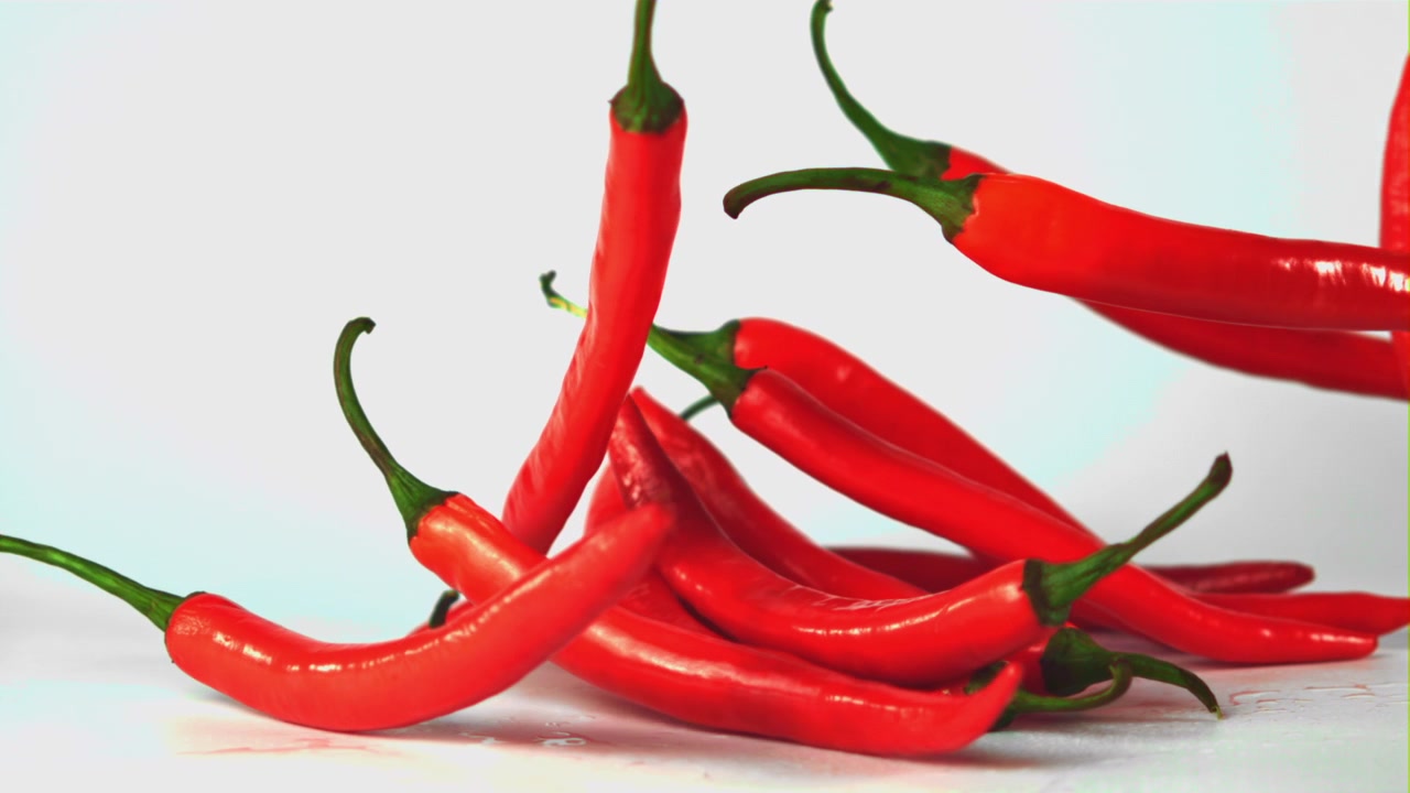 Red Chili Peppers Falling in Slow Motion on White Background