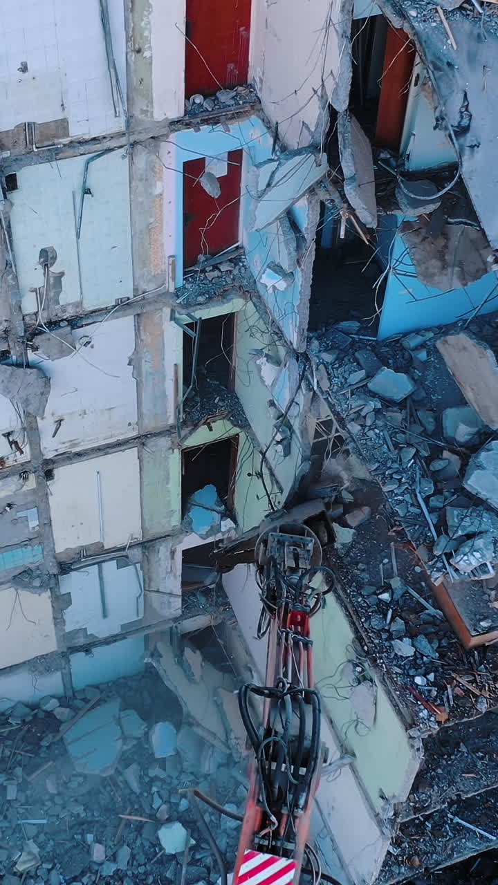 Heavy machinery dismantling the old building. Excavator disassembling the ruins of the construction. View from above. Vertical video