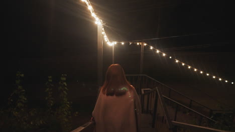 woman walking up stairs at night with string lights