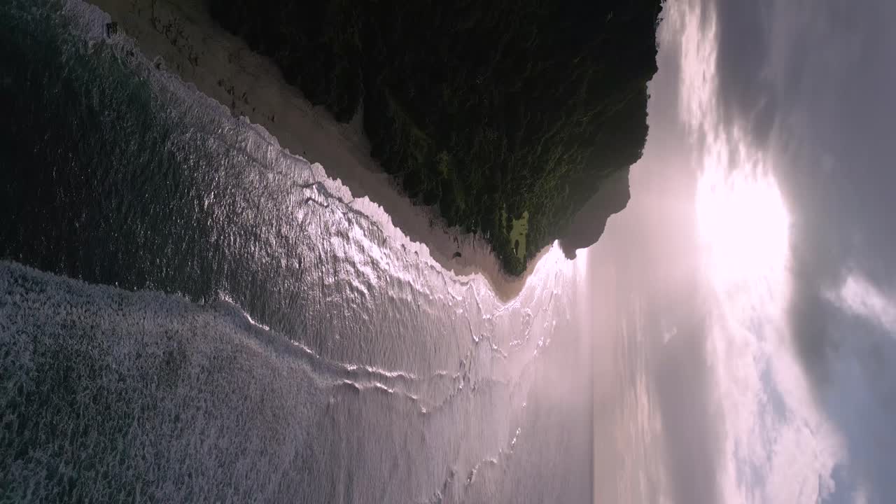olas en la playa mientras el sol brilla a través de las nubes