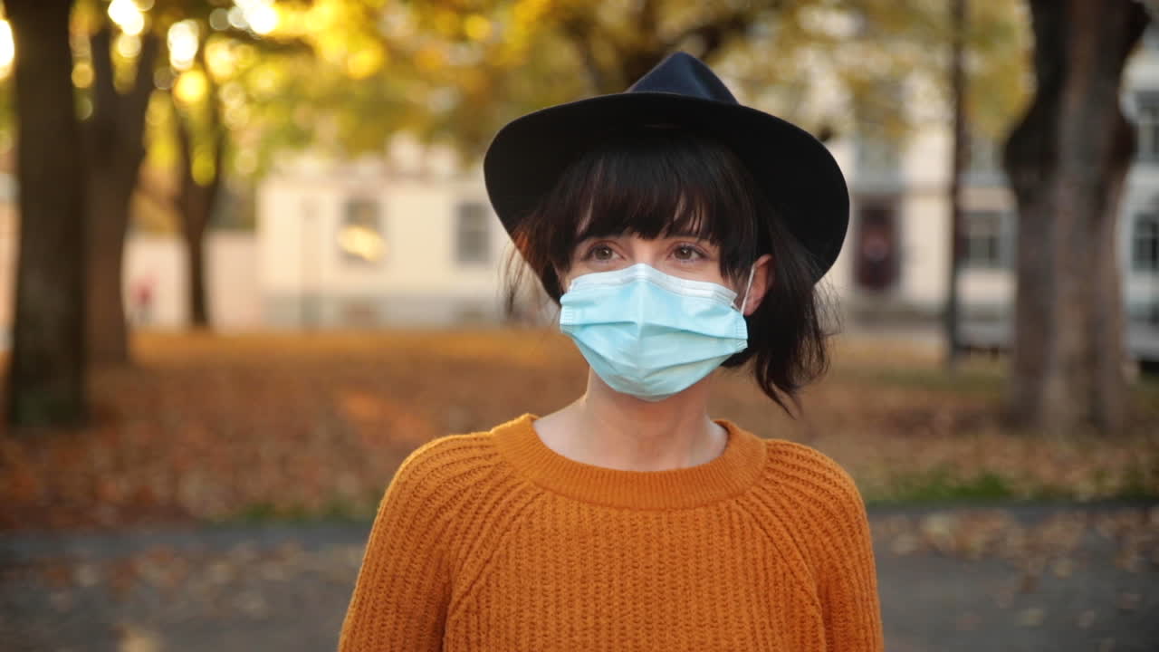 Young brunette woman walking under trees in autumn, wearing a mask during corona