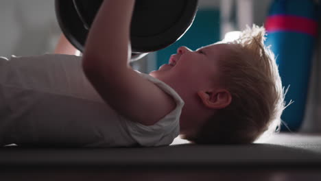Motivated-toddler-tries-hard-to-lift-heavy-barbell-in-gym