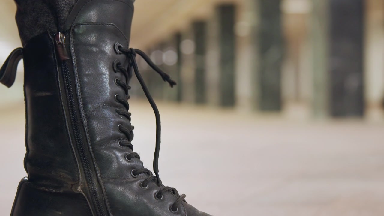 Individuo concentrado se abrocha los zapatos oscuros en el exterior. Viajero solitario ajusta calzado resistente en la calle de la ciudad. Explorador decidido asegurándose de que las botas de cuero negras estén bien ajustadas en el pavimento agrietado.