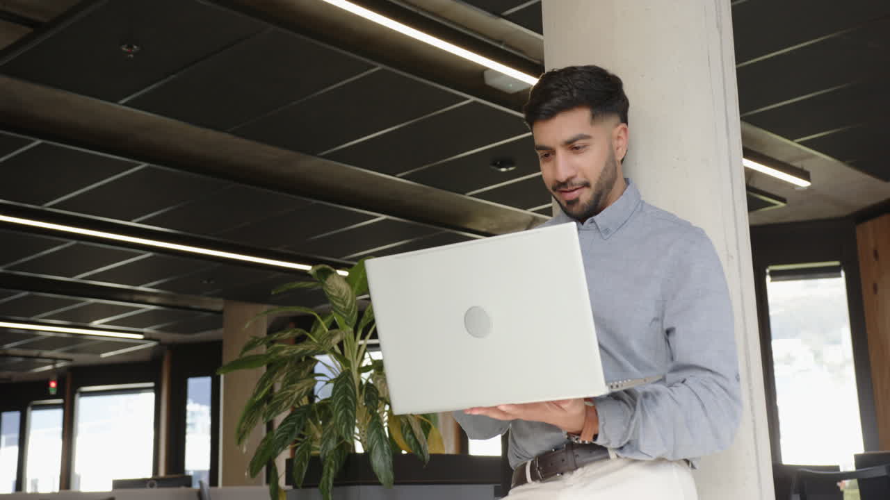Using laptop, Indian man working in modern office with plants and natural light