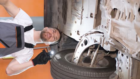 mechanic inspecting a car's undercarriage with a flashlight and wrench