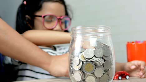 niña asiática poniendo la moneda en un frasco de vidrio profundidad poco profunda del campo seleccionar centrarse en el frasco