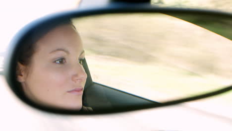 young woman driving in a car, reflection in rear-view mirror