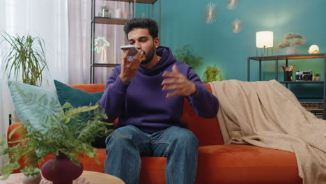 happy excited indian man making phone conversation talking with friend sitting call on couch at home