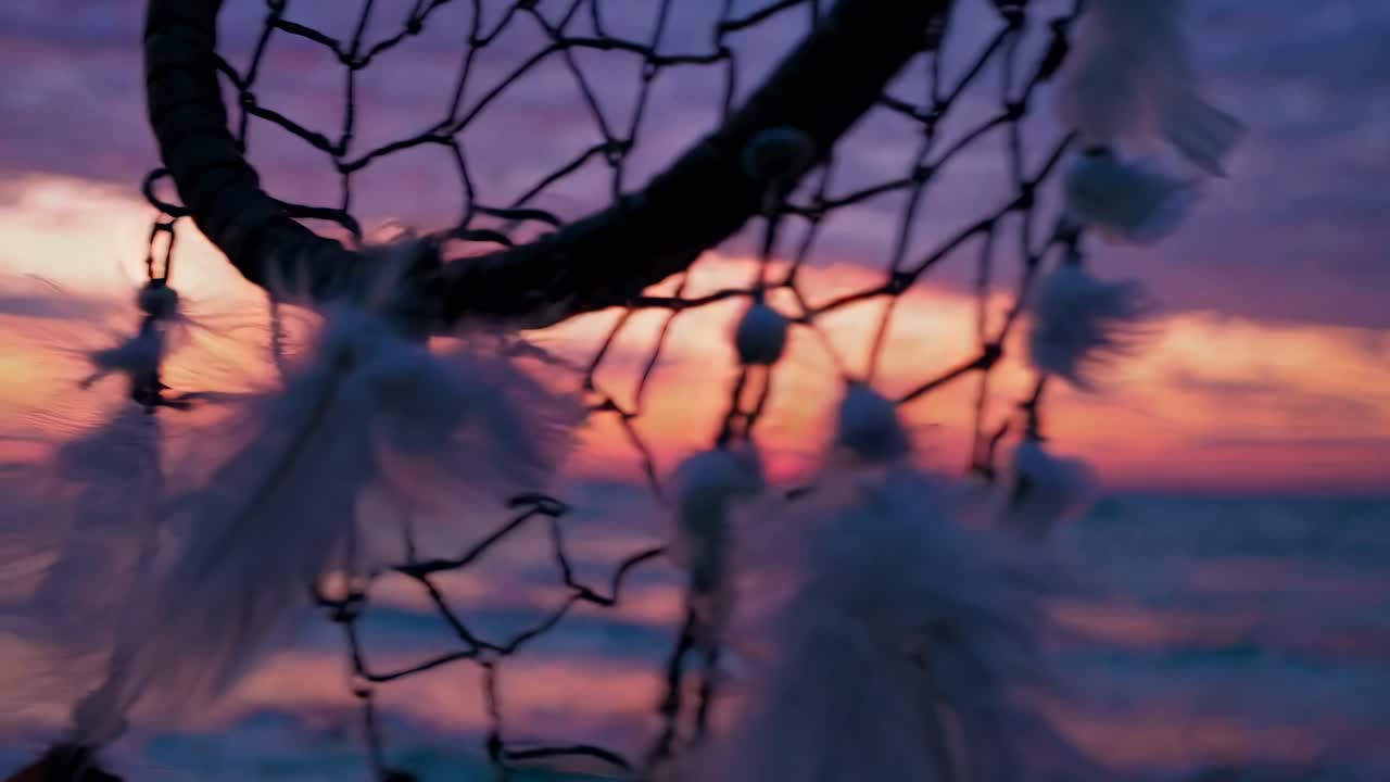 Acchiappasogni con piume sullo sfondo di un tramonto vivido sull'oceano.