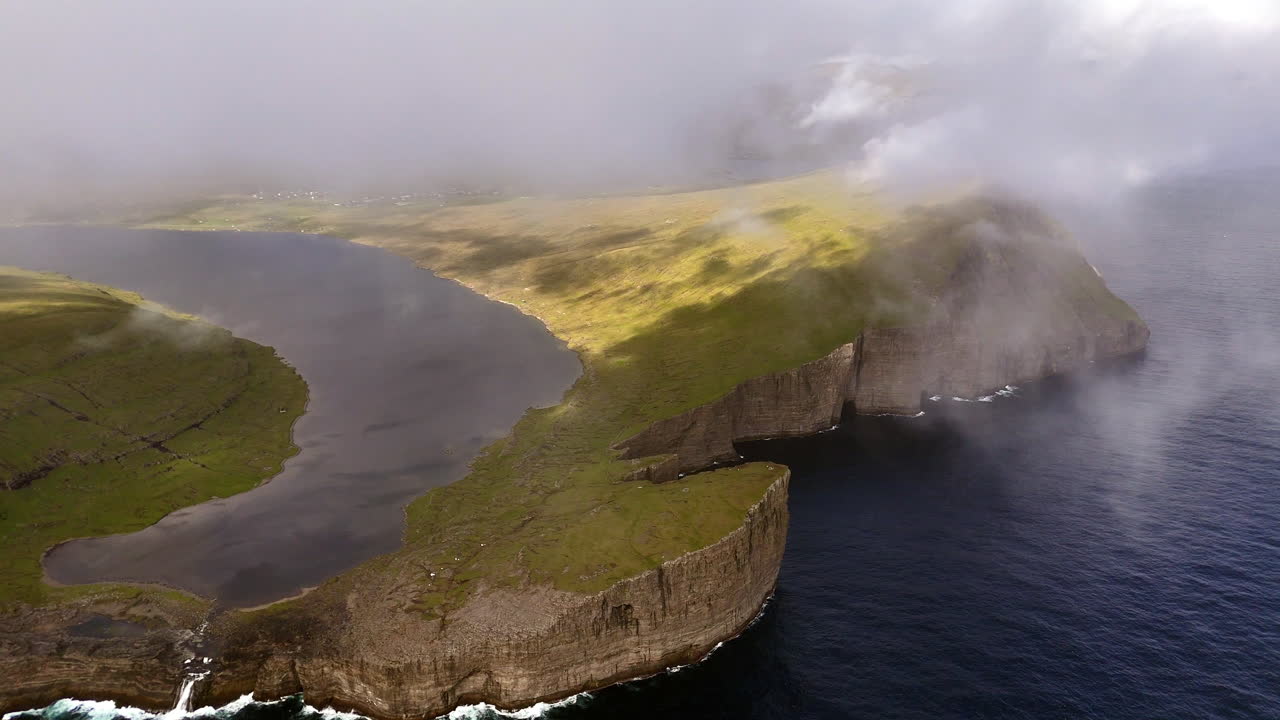 Aerial view of dramatic cliffs and coastline at Lake Sørvágsvatn, Faroe Islands, with rolling clouds, rugged landscape, and the Atlantic Ocean horizon