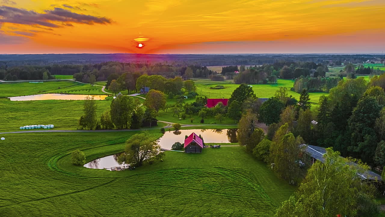 Panoramica dall'alto di una casa vicino a un laghetto con persone che mangiano all'aperto mentre il sole tramonta e illumina di giallo il cielo nuvoloso