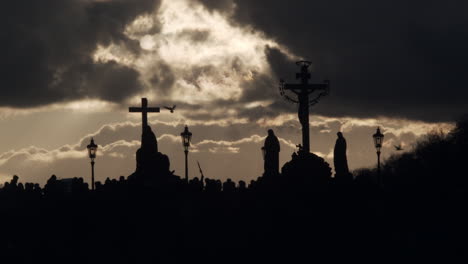 Silhouettes-of-tourists-pass-Charles-Bridge-statues-in-Prague-dusk,-wide