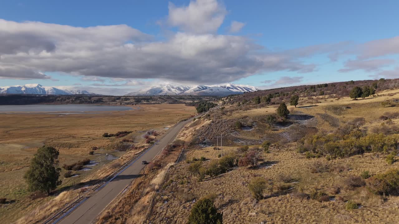 Provincial Route 71 crossing the vast Patagonian plains in Chubut Province, Argentina, with distant Andres snow-capped mountain ridge under a partly cloudy sky on a crisp, clear morning drone shot