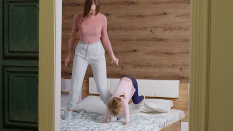 young lovely mother babysiter and little kid daughter jumping dancing on bed in modern house bedroom