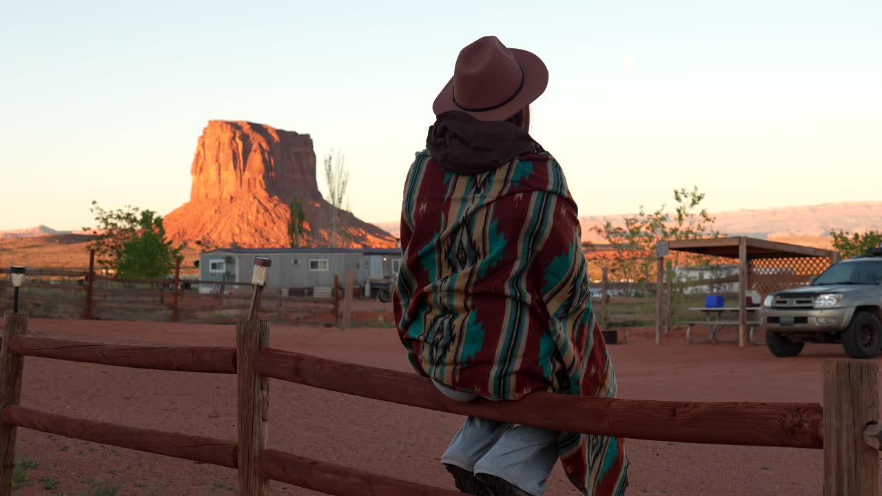 Person in Hat and Blanket Sitting on Fence Overlooking Desert Landscape