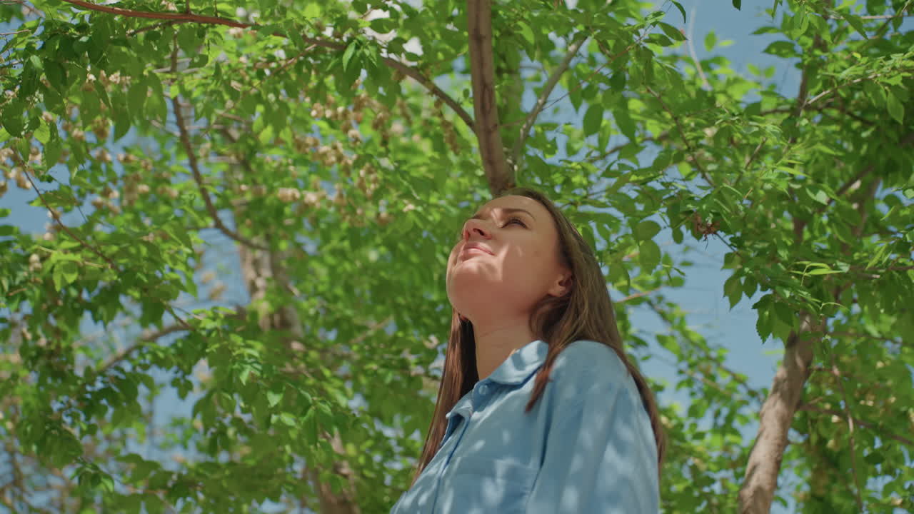 parque veraniego tranquilo, una señora serena ajustándose las gafas de sol en el exterior, una mujer relajada en vaqueros disfrutando de la sombra y la luz del sol, una mujer elegante con top vaquero saboreando el ambiente tranquilo del parque con luz tenue