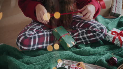 woman opening red ribbon on wrapped christmas gift at home