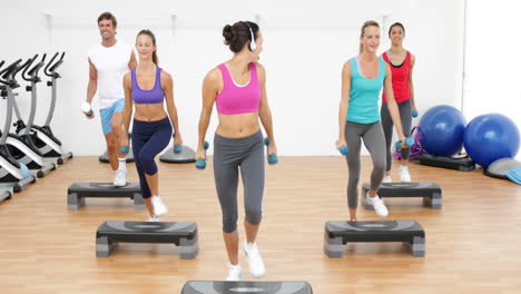 clase de aeróbica dando pasos juntos dirigida por un instructor y levantando pesas