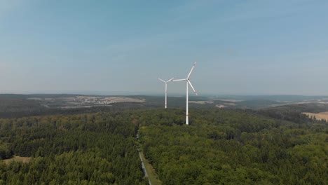 Wide-aerial-shot-if-a-wind-farm-in-the-German-countryside,-turbines-spinning-on-a-a-bright-sunny-day