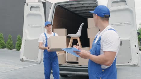 two young workers of removal company unload boxes and furniture from minibus into customer's home