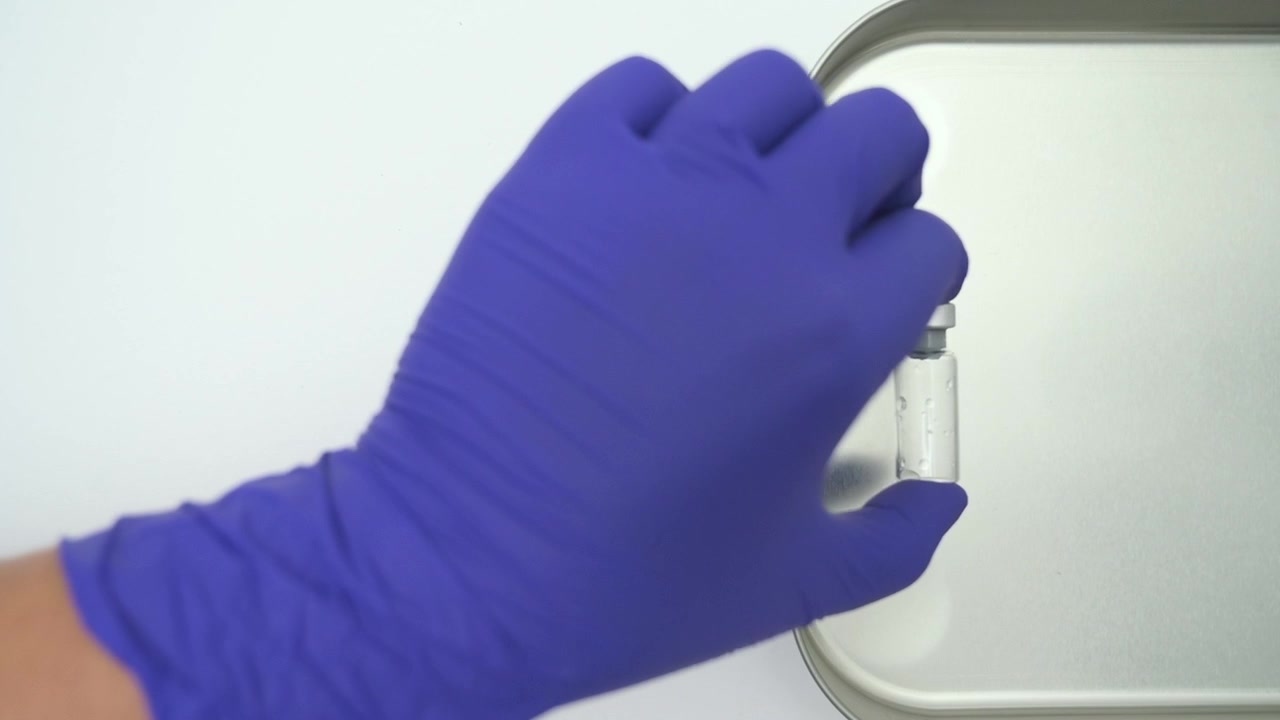 Operatore sanitario con guanti chirurgici blu che prende una fiala di vetro trasparente per la vaccinazione.