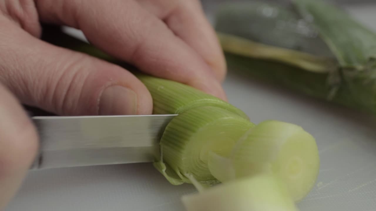 Hand slicing leek vegetable macro close up shot