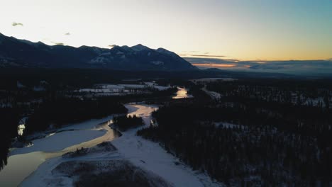 Exquisite-Winterlandschaft-Während-Der-Goldenen-Stunde:-Luftschwenk-Nach-Links-Von-Einem-Schimmernden-Fluss-Und-Eleganten-Bergen-In-Britisch-Kolumbien,-Kanada