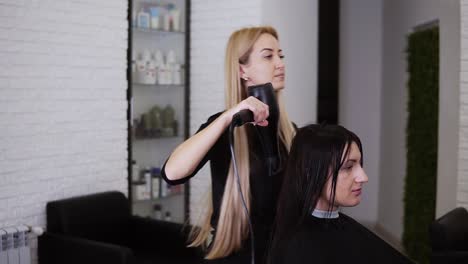 Kaukasische-Brünette-Junge-Frau-Lässt-Sich-Nach-Dem-Neuen-Haarschnitt-Im-Friseursalon-Von-Der-Kosmetikerin-Die-Haare-Trocknen.-Schönheitsindustrie.-Zeitlupe