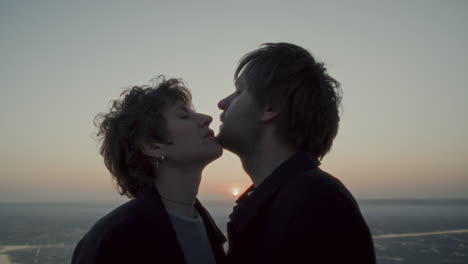 affectionate couple rubbing chins and kissing outdoors at sunset