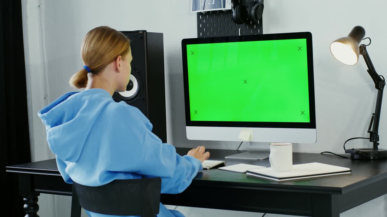joven sonriendo mirando a la cámara sentada frente a un monitor verde