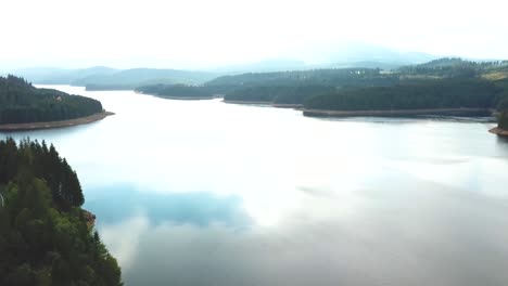 Toma-Panorámica-Hacia-Adelante-Sobre-Un-Lago-En-Un-Día-Nublado,-Bosque-En-El-Fondo-Brumoso