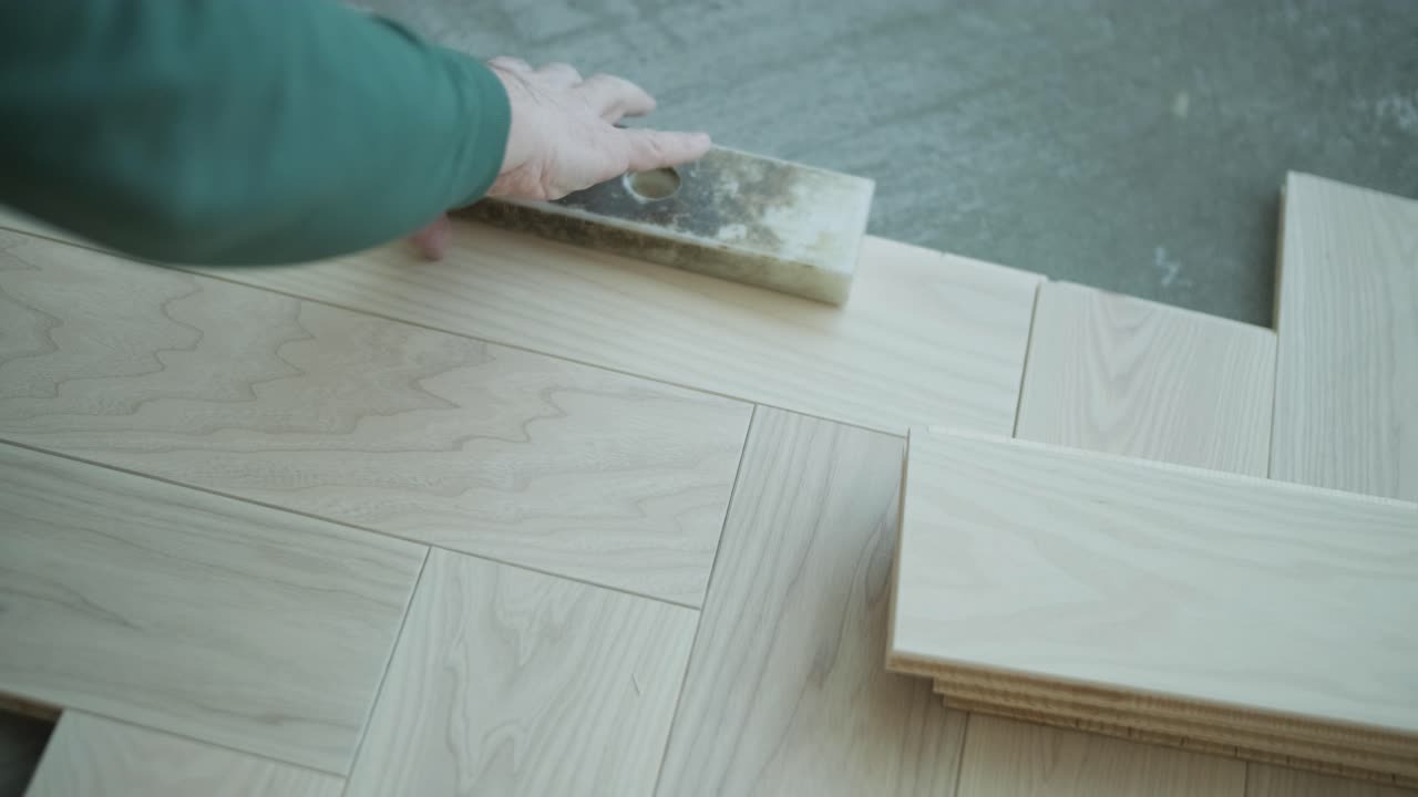 Worker installing wooden flooring with hammer and tapping block