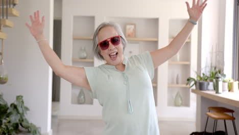 excited asian grandmother wearing sunglasses, raising arms and smiling at home