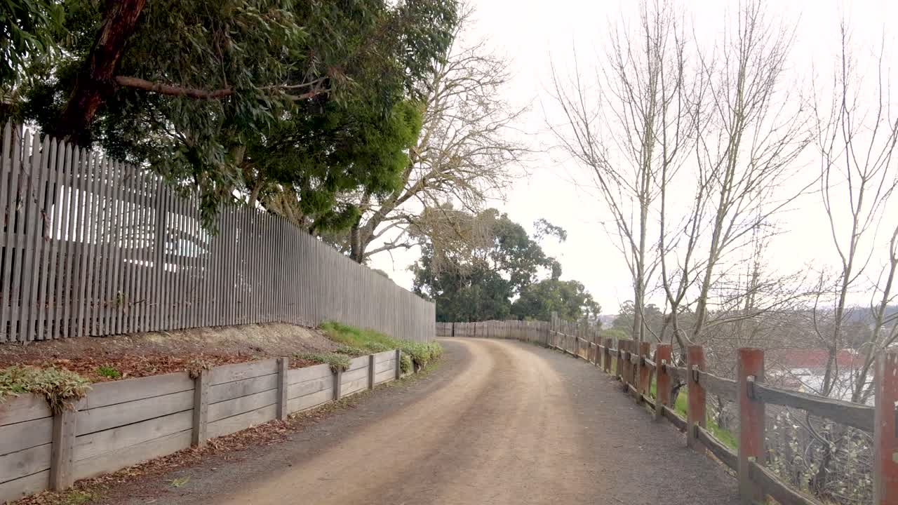 A peaceful dirt path lined with trees and a wooden fence in Melbourne, captured in natural daylight with a serene atmosphere