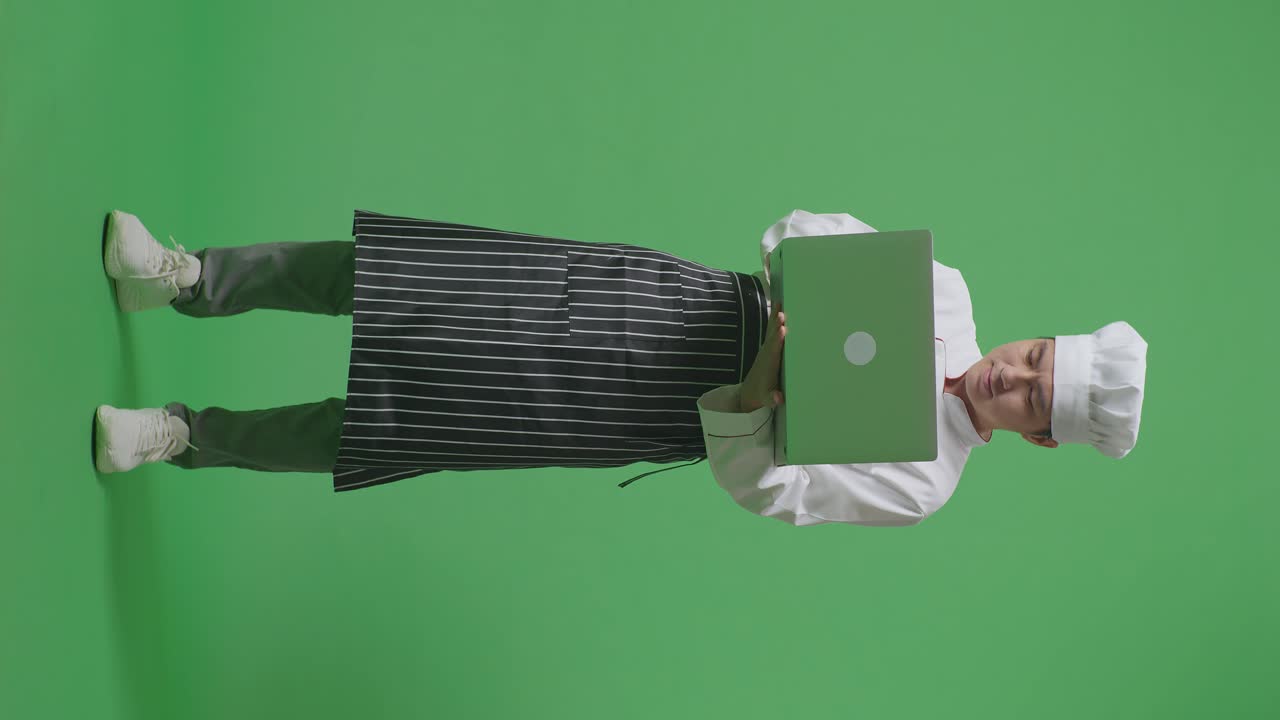 Full Body Of Asian Man Chef Using A Laptop While Standing In The Green Screen Background Studio