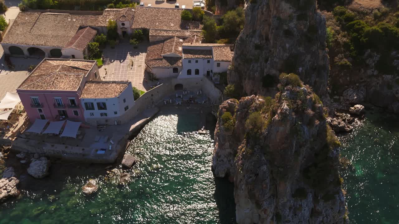 Aerial drone flying over Tonnara di Scopello, Sicily, Italy, showcasing its rocky coastline, turquoise waters, and historic tuna fishery during Italian summer, with scenic views of cliffs