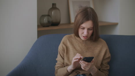 business-woman-typing-message-on-mobile-phone-at-home-office.-Young-girl-chatting-on-phone-in-slow-motion.-Close-up-young-woman-hands-using-smartphone-on-couch.