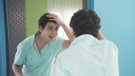 A-handsome-young-man-with-curly-hair-is-happy-looking-at-himself-in-the-mirror.