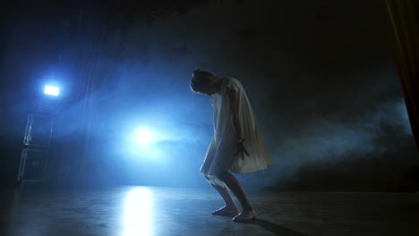 a dramatic scene of modern ballet a lone ballerina in a white dress performs dance steps using modern choreography.