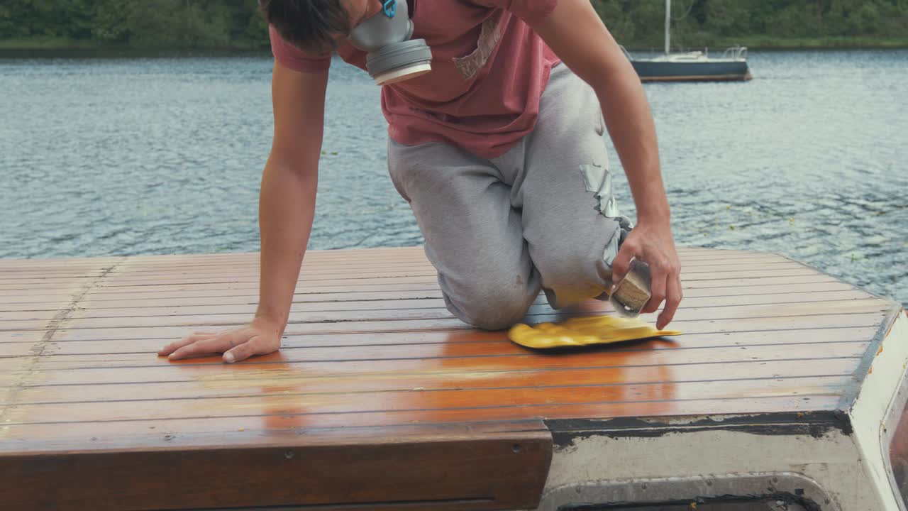 Young man manually sanding roof planking of boat