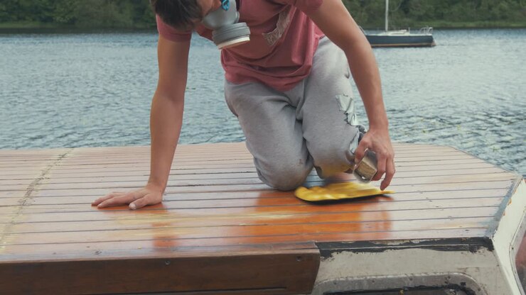 Young man manually sanding roof planking of boat