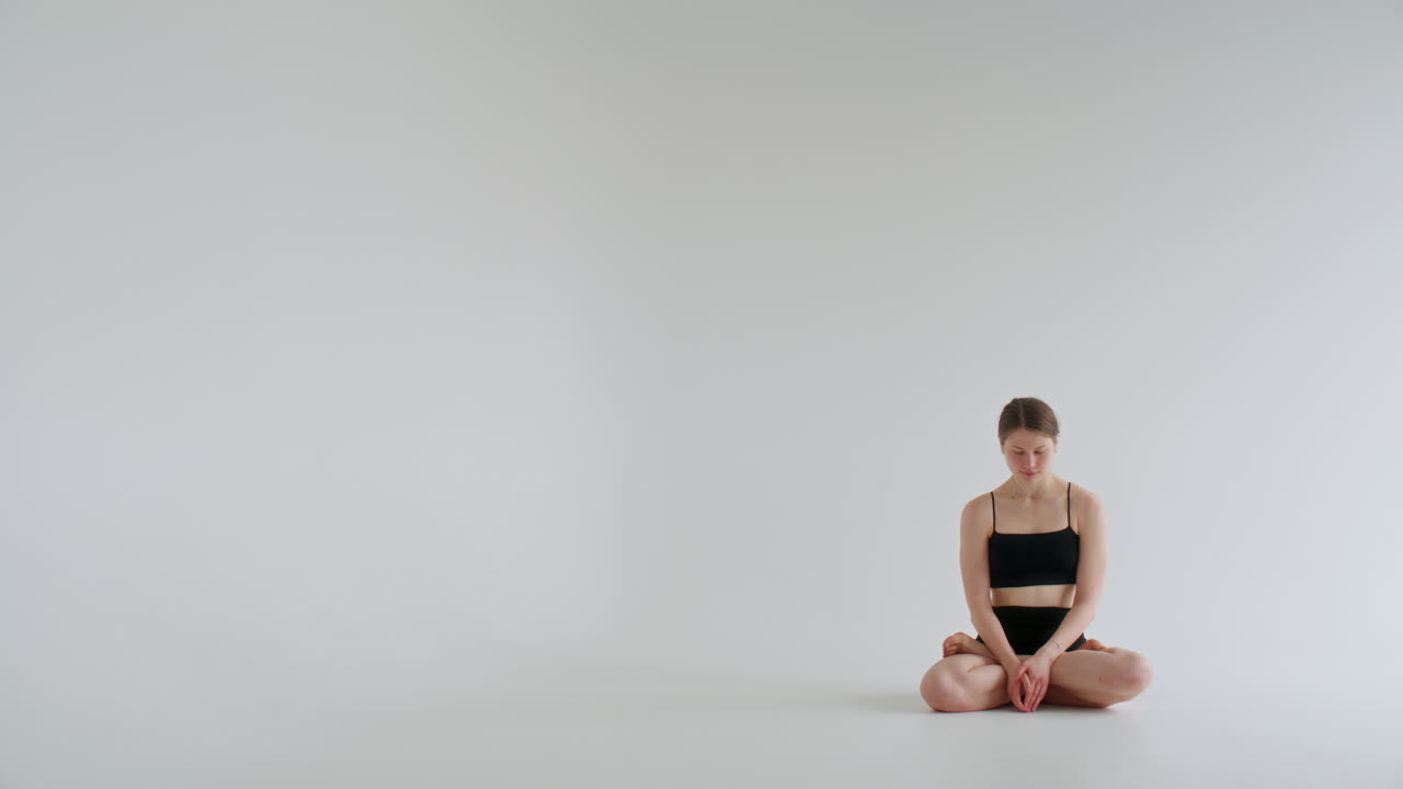 Giovane donna che medita nella posizione del loto con le mani in Namaste in uno studio bianco