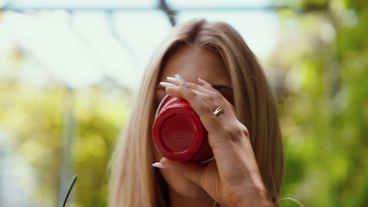 attractive woman drinking from a red cup close up in a park or garden