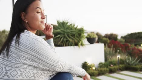retrato de una mujer biracial sonriente sentada y admirando la vista en el jardín, en cámara lenta